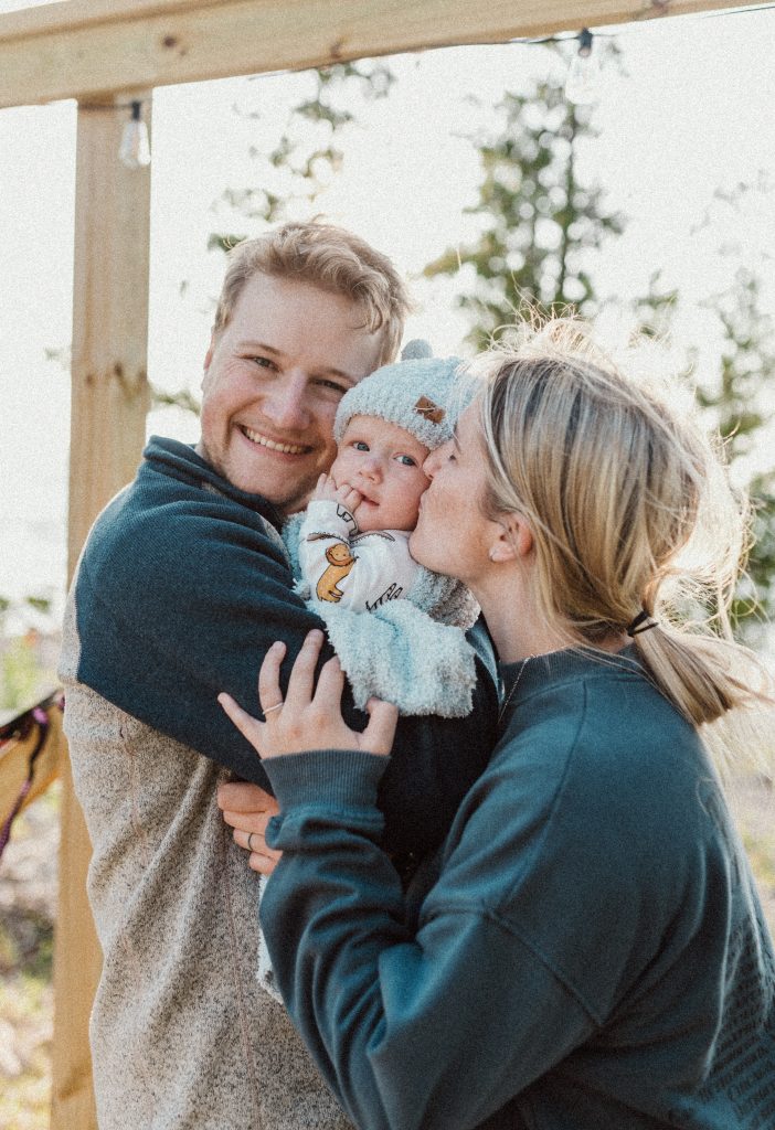 Smiling young family holding their baby at their cozy campsite at Butter & Grahams on Drummond Island, enjoying a sunny summer adventure.